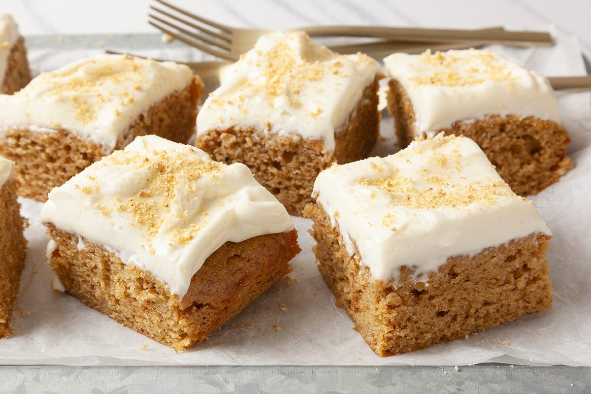 Six frosted cake squares on parchment paper, topped with creamy white icing and sprinkled with a crumb garnish. 