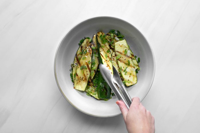 Grilled zucchini in a large bowl with green onions, lemon juice, salt, pepper flakes and remaining oil
