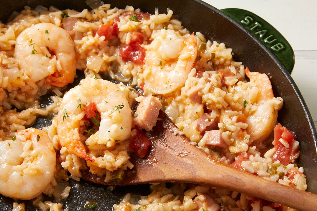 overhead closeup shot of Ham and Shrimp Jambalaya in a deep skillet; a wooden spoon rests atop the mixture