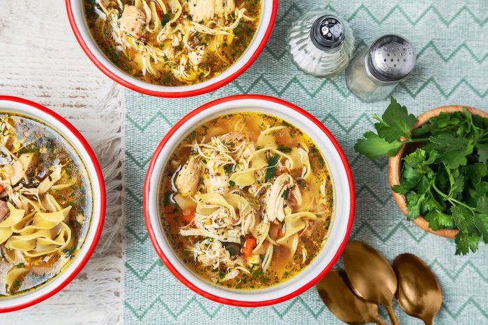 Cover push pull image of Taste of Home's Instant Pot Chicken Noodle Soup shot on a white wooden surface. Soup served in white and red enamel bowls with chopped fresh parsley as garnish; overhead
