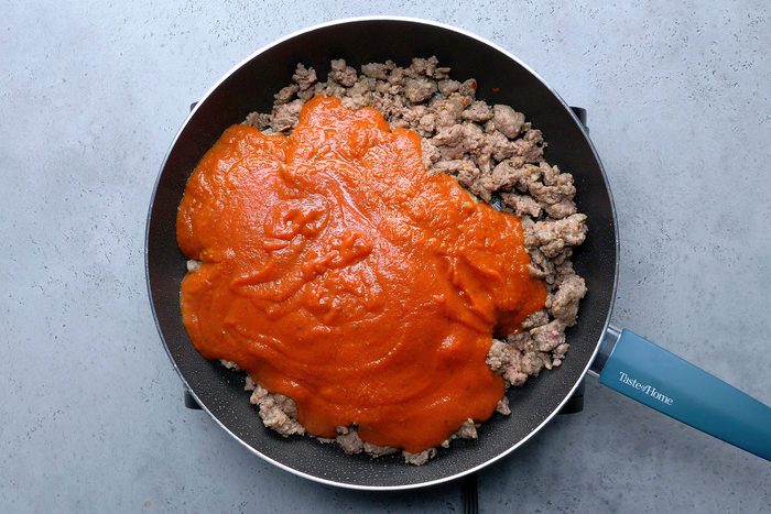 Overhead shot of a large skillet; cook and crumble beef and sausage over medium-high heat until no longer pink; drain; Stir in marinara and pizza sauces; induction stove; grey surface;