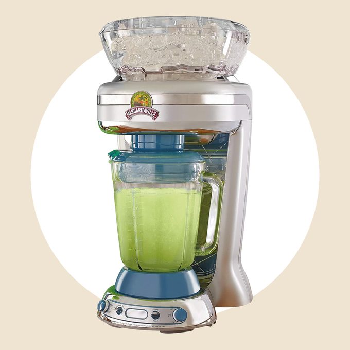 A margarita machine with a clear container of ice at the top and a pitcher filled with a lime green liquid. The base has buttons and a metallic finish, set against a circular white background.