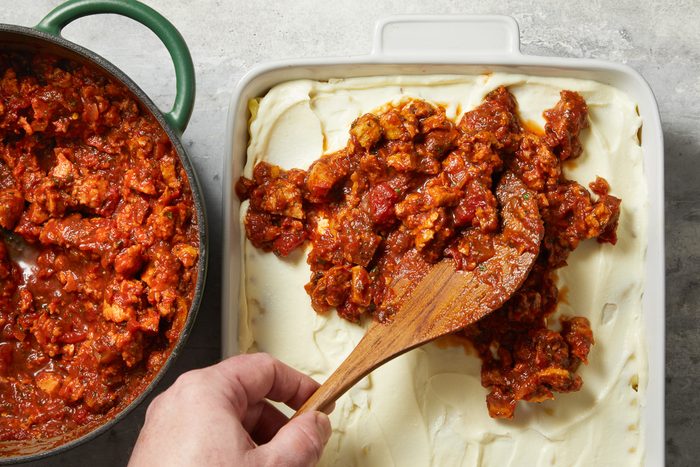 meat sauce being added on top of riccota mix spread