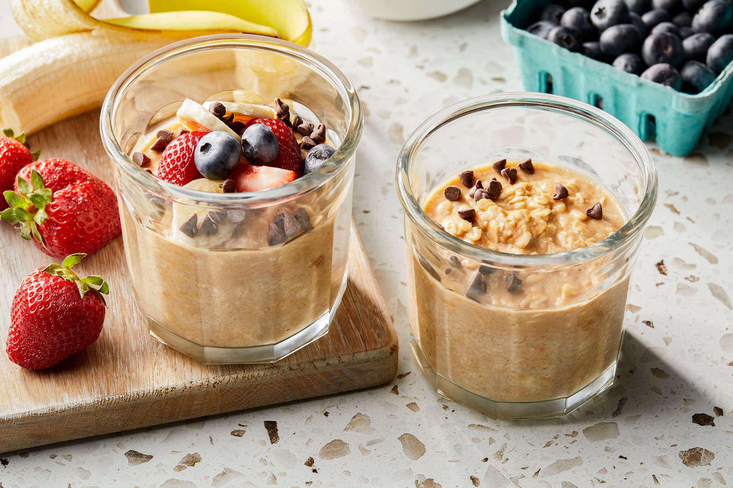 Peanut Butter Overnight Oats in glass containers with fruit toppings and strawberry and blueberries on side