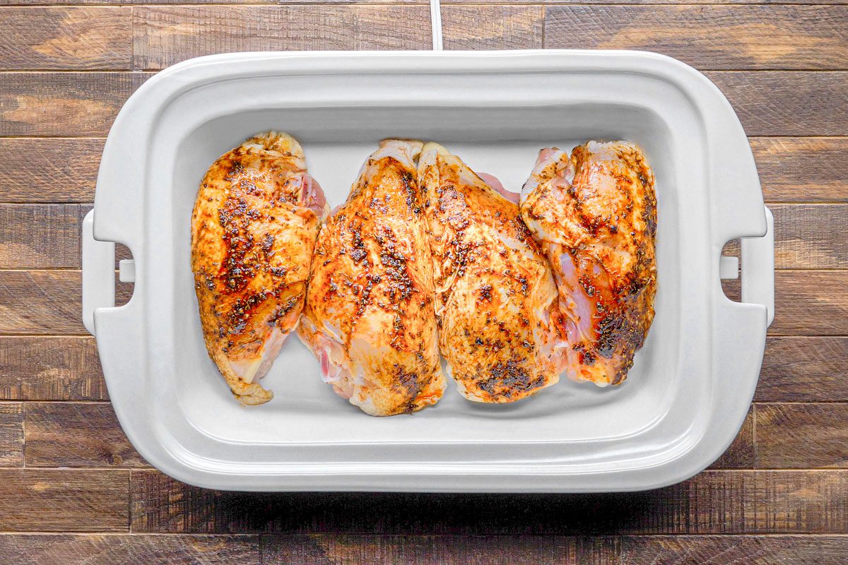 overhead shot of four pieces of chicken breast in a white oval-shaped dish; the dish is sitting on a wooden surface; the chicken breast is seasoned with herbs and spices and appears to be cooked