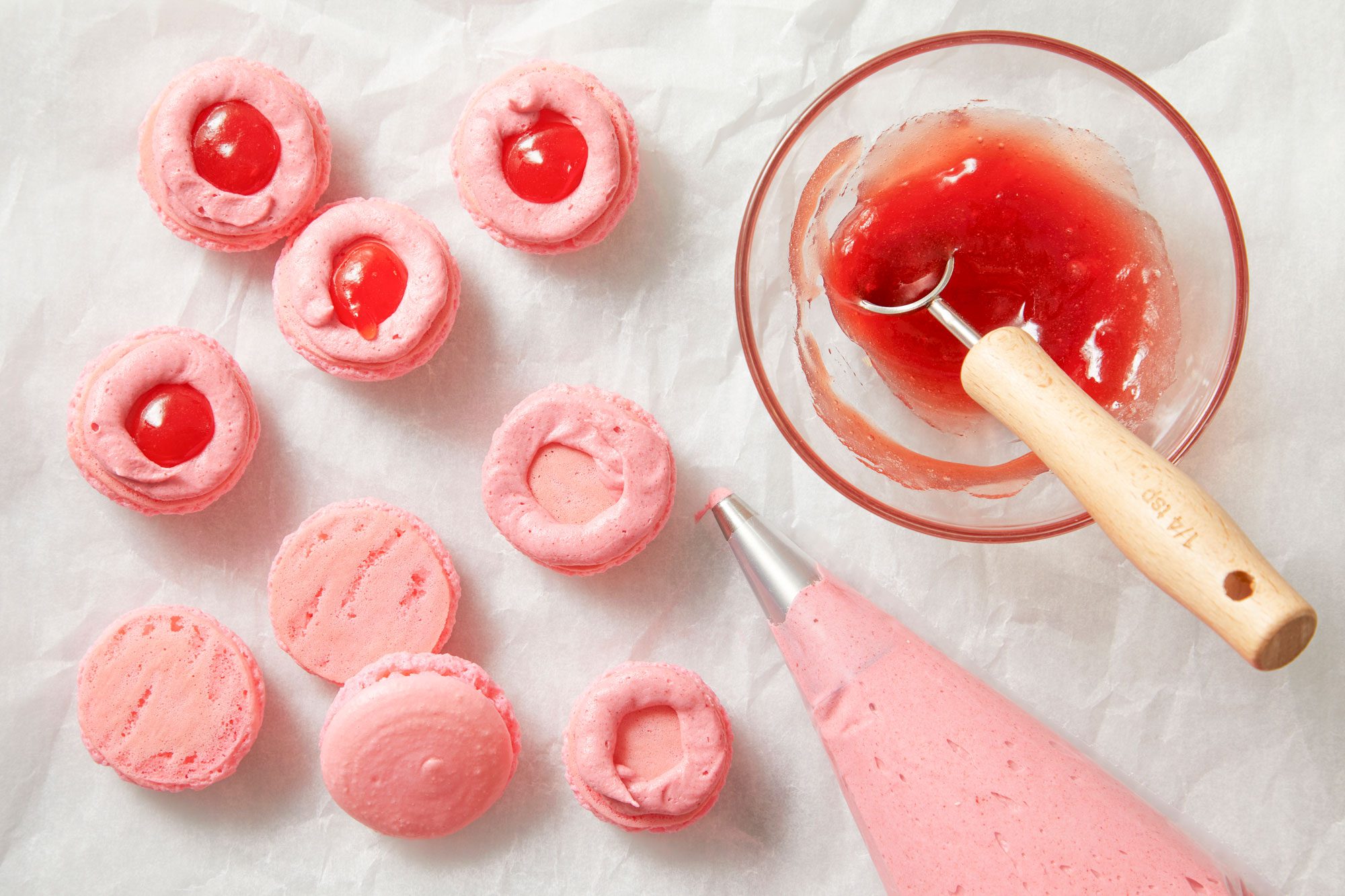 Overhead shot of pour frosting into a pastry bag fitted with a small round tip; pipe a circle of buttercream onto the bottoms of half the macarons; Place 1/4 teaspoon strawberry jam in center of each frosting circle; Top with remaining macaron shells; refrigerate covered until ready to serve;