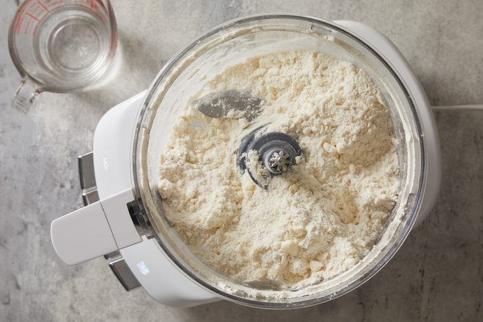 Overhead shot of place flour and butter in a food processor; pulse until butter is the size of peas; marble surface;