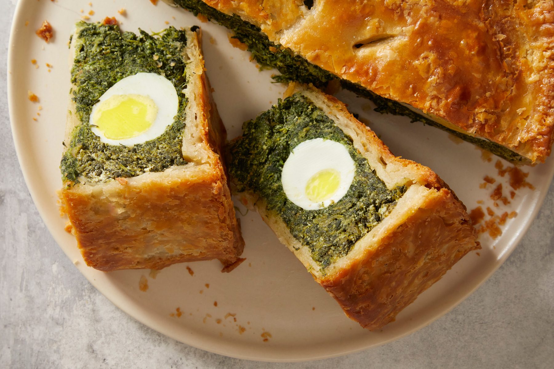 Overhead shot of Torta Pasqualina; placed on a large plate; cut into pieces; all set on marble surface;