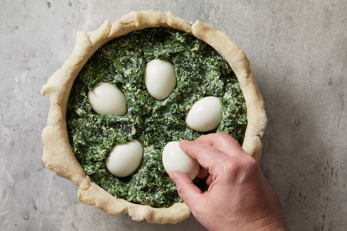 Overhead shot of place the hard-boiled eggs in an evenly spaced circle; pressing them down into the spinach filling; marble surface;