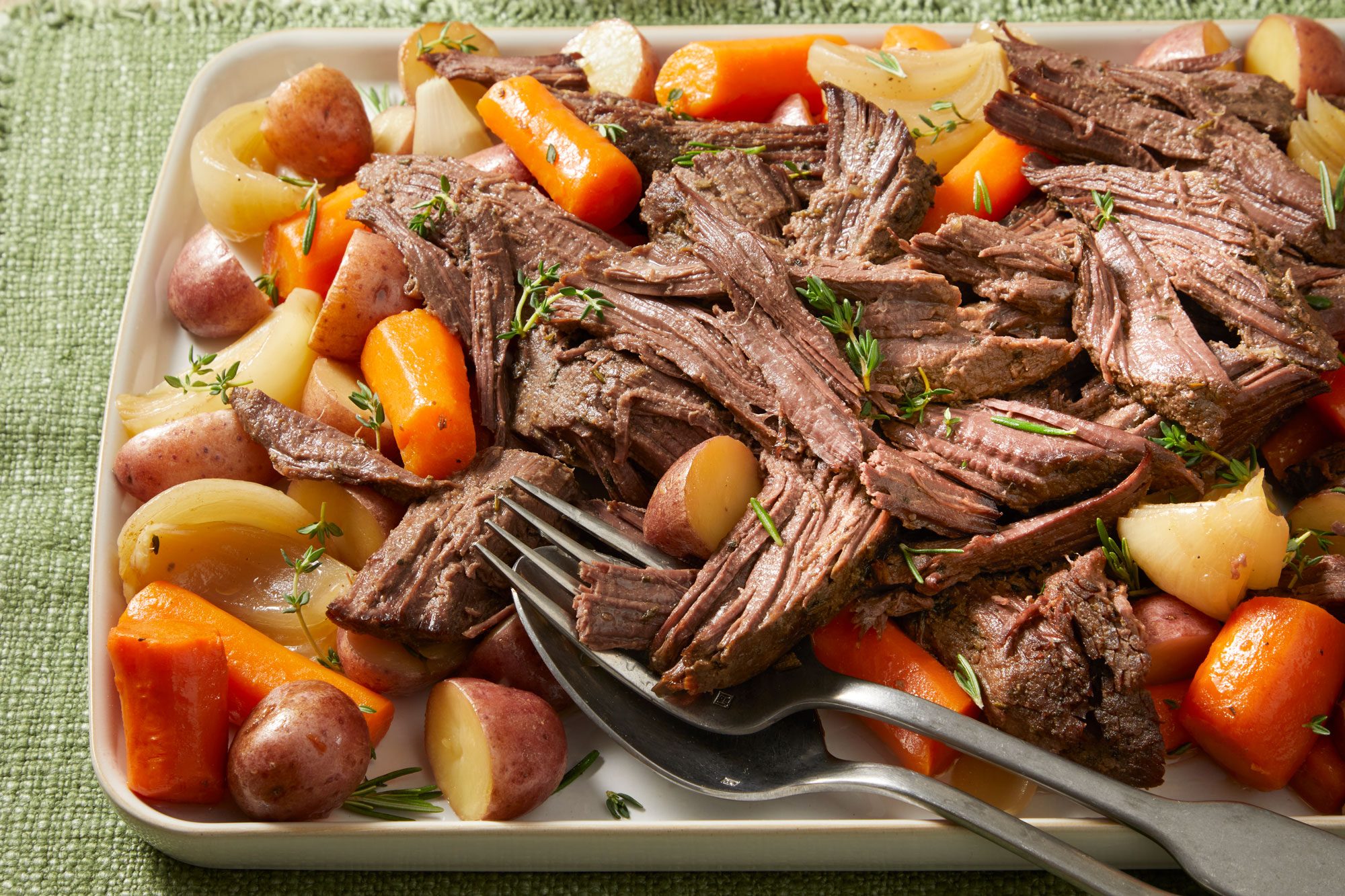Close shot of Venison Roast; served in a large plate with spoon and fork; on a green tablecloth;