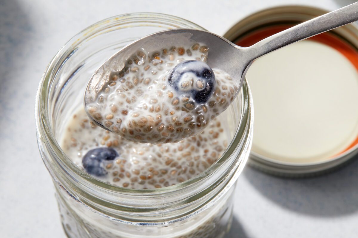 A glass jar filled with chia seed pudding and blueberries, with a spoon lifting out a portion. The jar