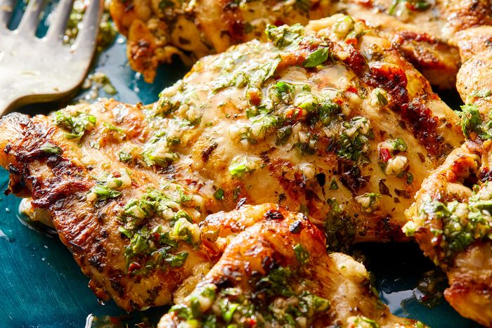 closeup shot of Chimichurri Chicken, plated on a turquoise oval dish; a fork rests beside the chicken