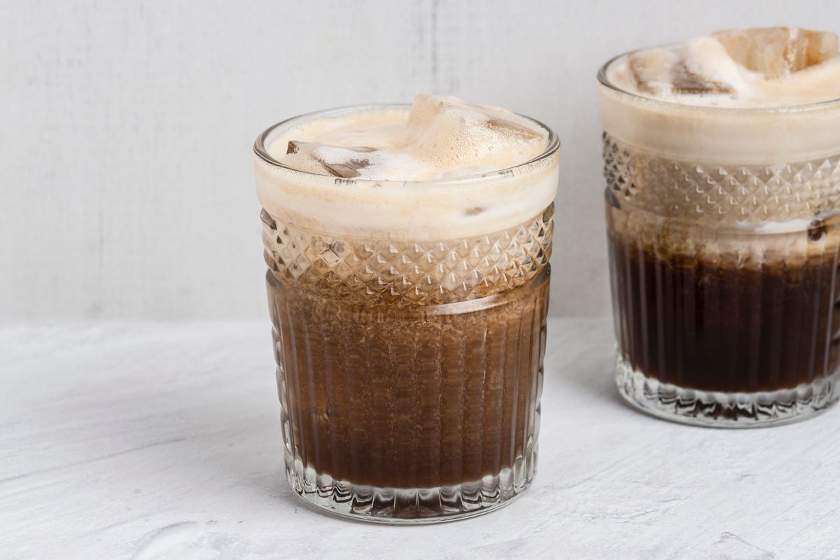 Table view shot; Add ice to a 16-ounce glass; Pour espresso mixture over the ice; top with oat milk; Serve immediately; white surface;