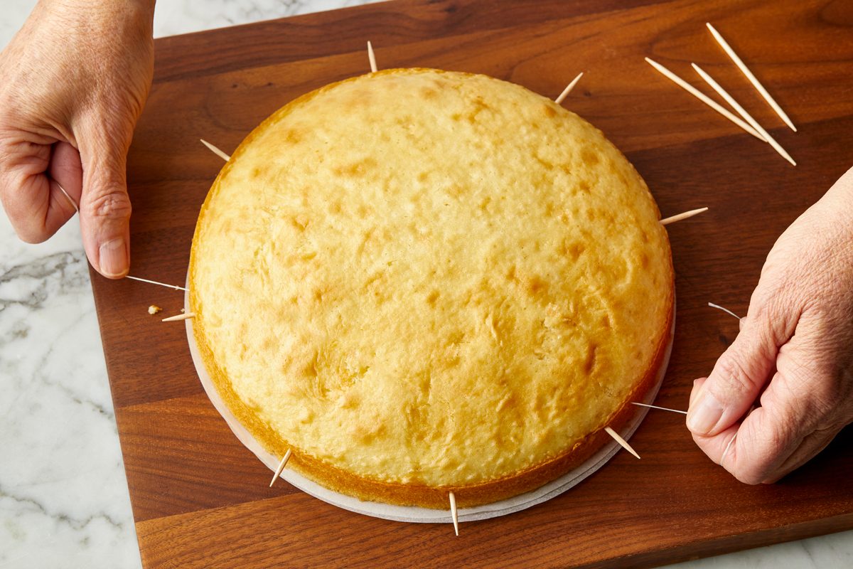 Two hands cutting a cake layer with dental floss over a wood cutting board with a marble surface.