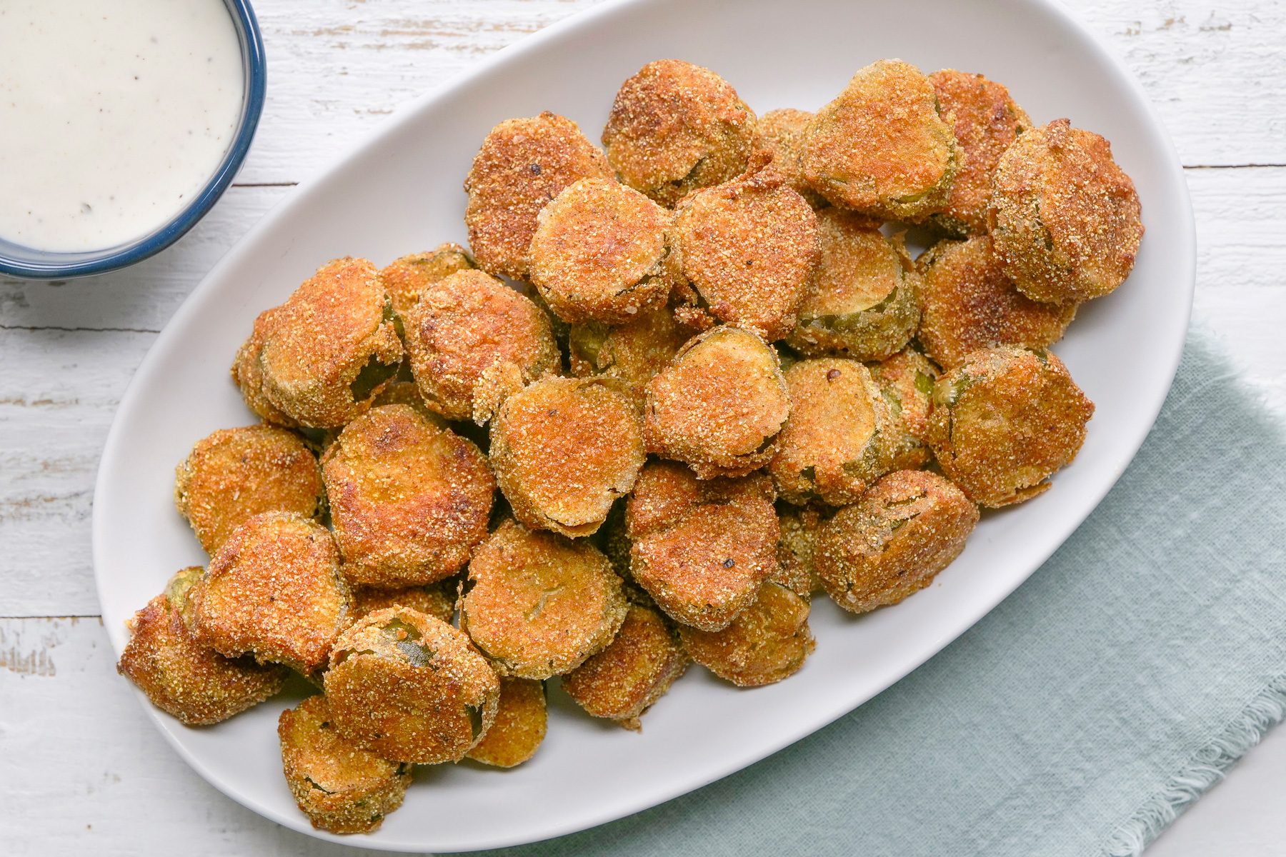 Overhead shot of Fried Dill Pickles; served on large platter with sauce bowl; a napkin; white wooden surface;