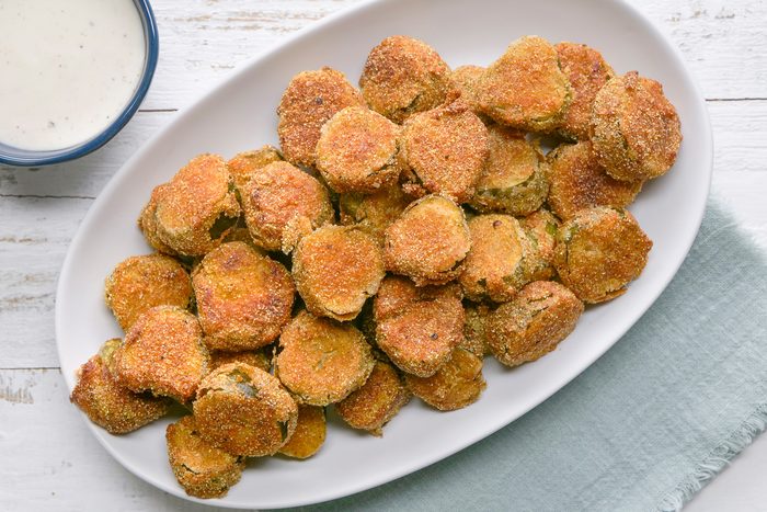 Overhead shot of Fried Dill Pickles; served on large platter with sauce bowl; a napkin; white wooden surface;