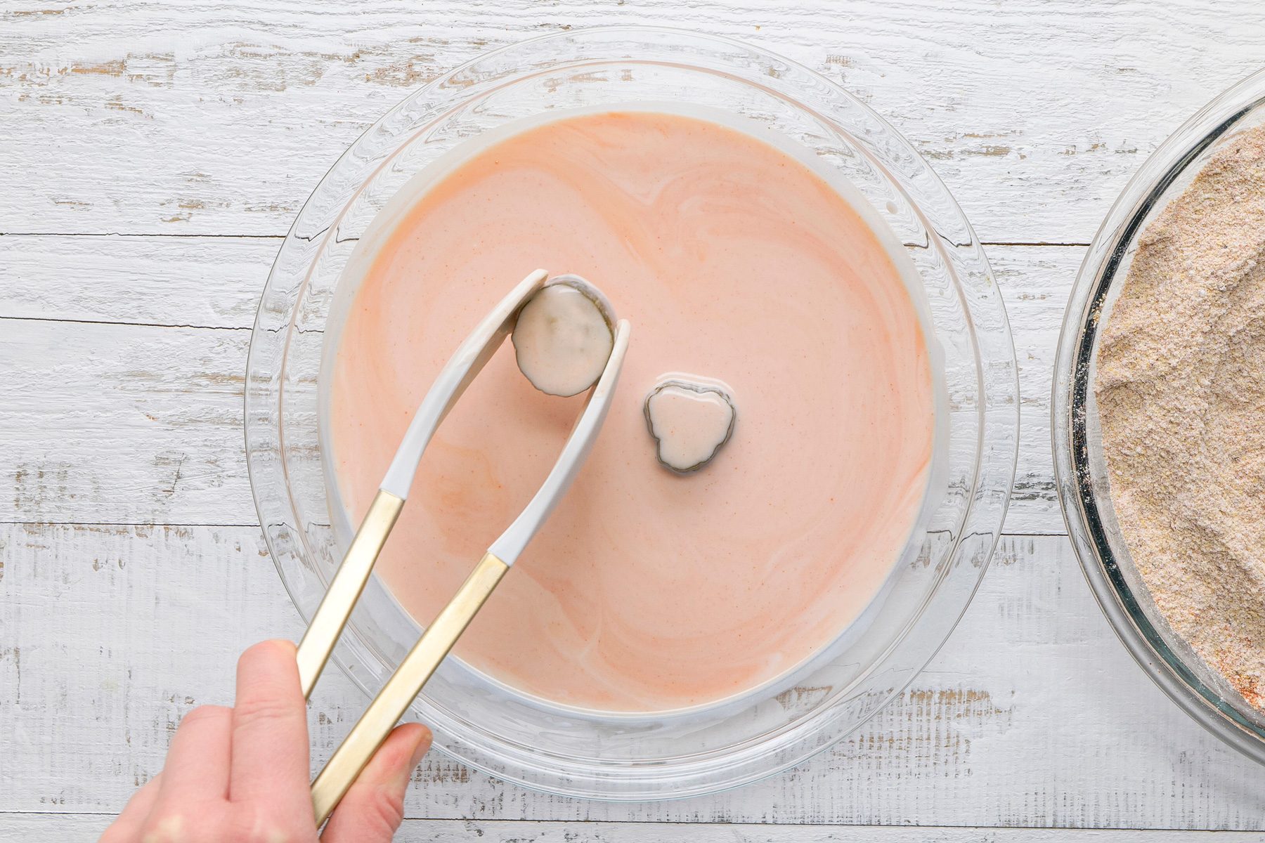 Overhead shot of dip pickles in buttermilk mixture; white wooden surface;