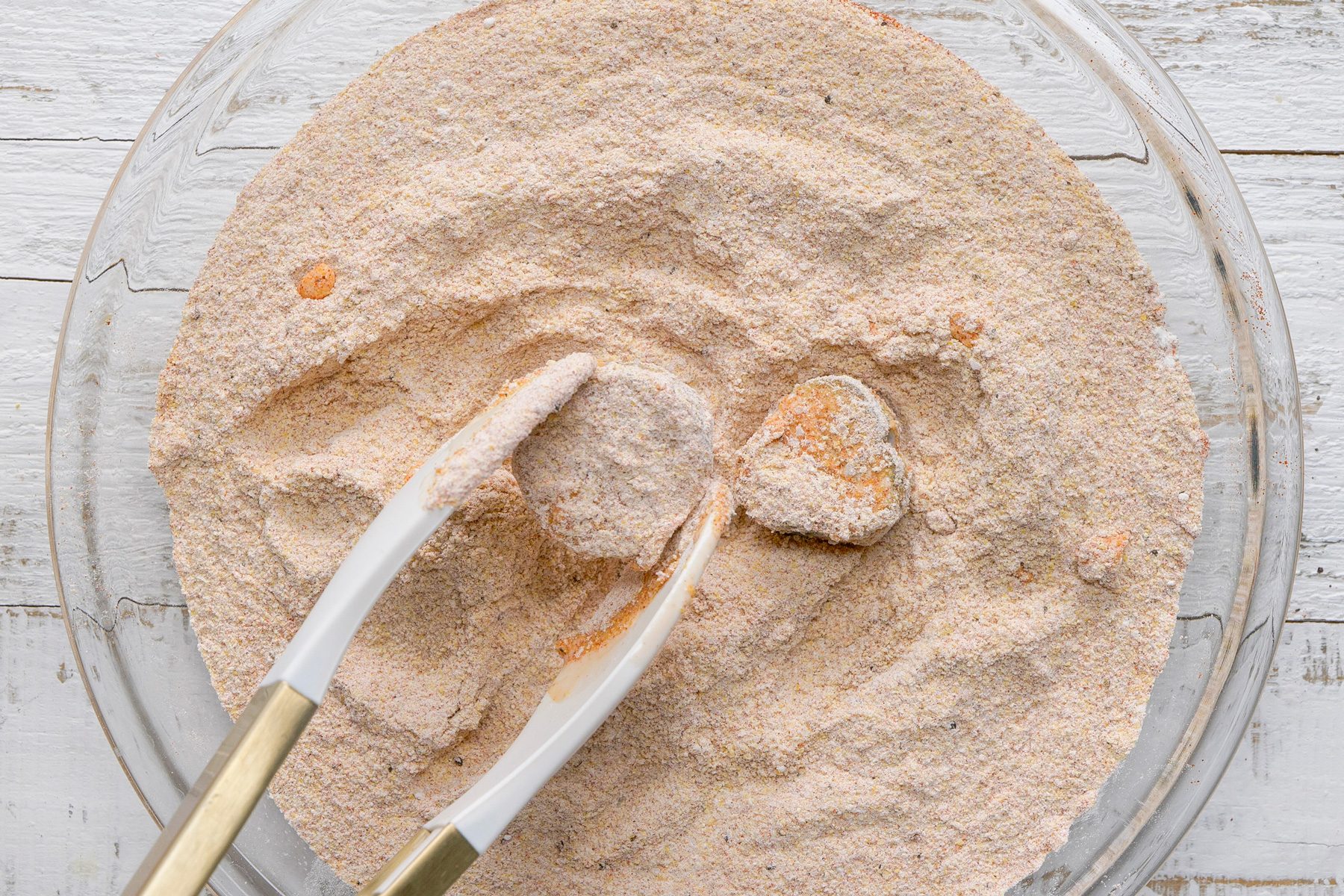 Overhead shot of dip in flour mixture; tongs; white wooden surface;