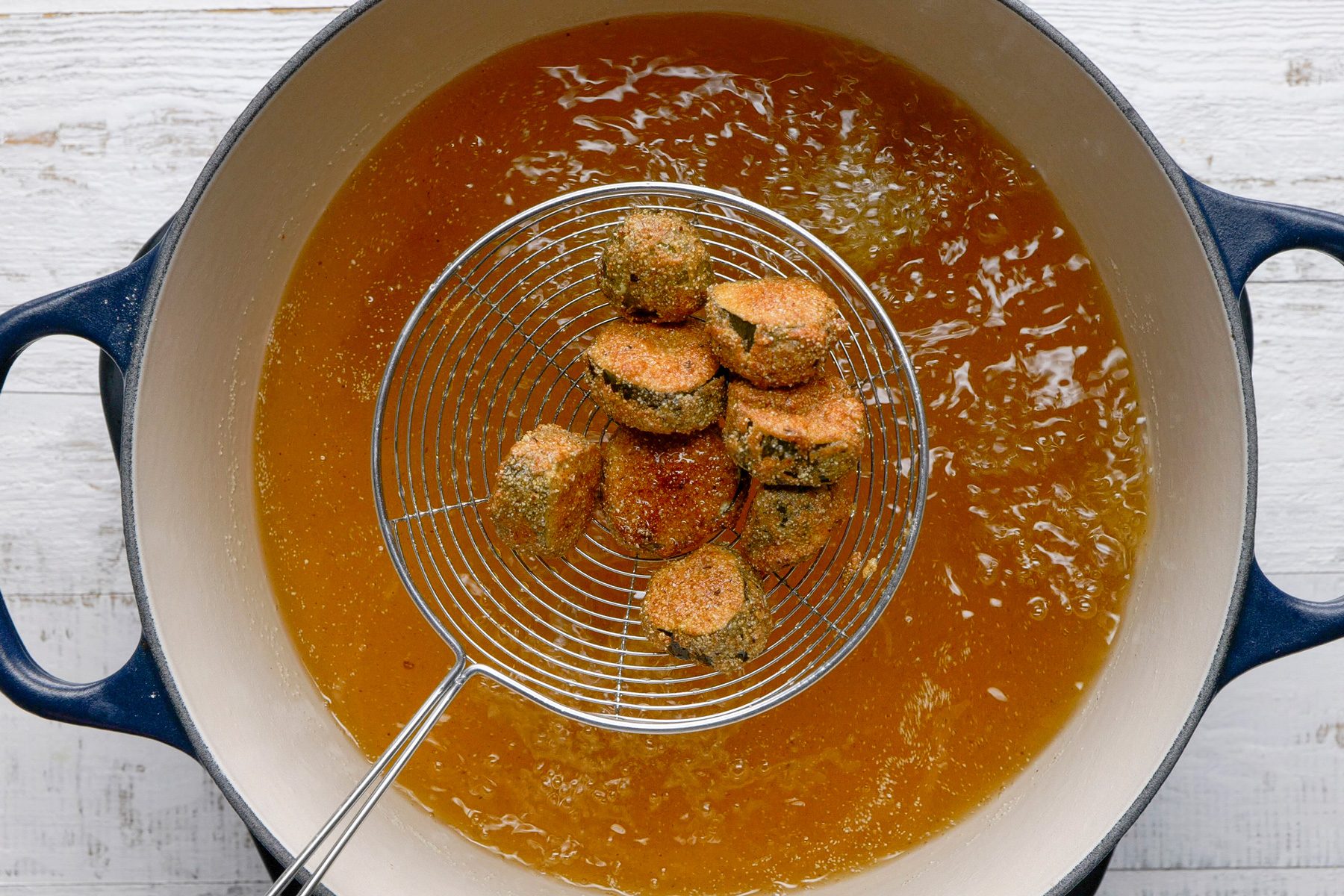 Overhead shot of a Dutch oven; heat 1 inch of oil to 375 degree; Working in batches; fry pickles 2-3 minutes on each side or until golden brown; Drain on paper towels; Serve immediately with ranch dressing; white wooden surface;