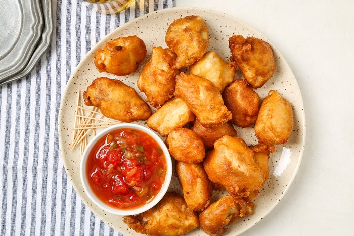 Fried Sweet And Sour Chicken in a cream plate on a striped kitchen towel with a sauce on side