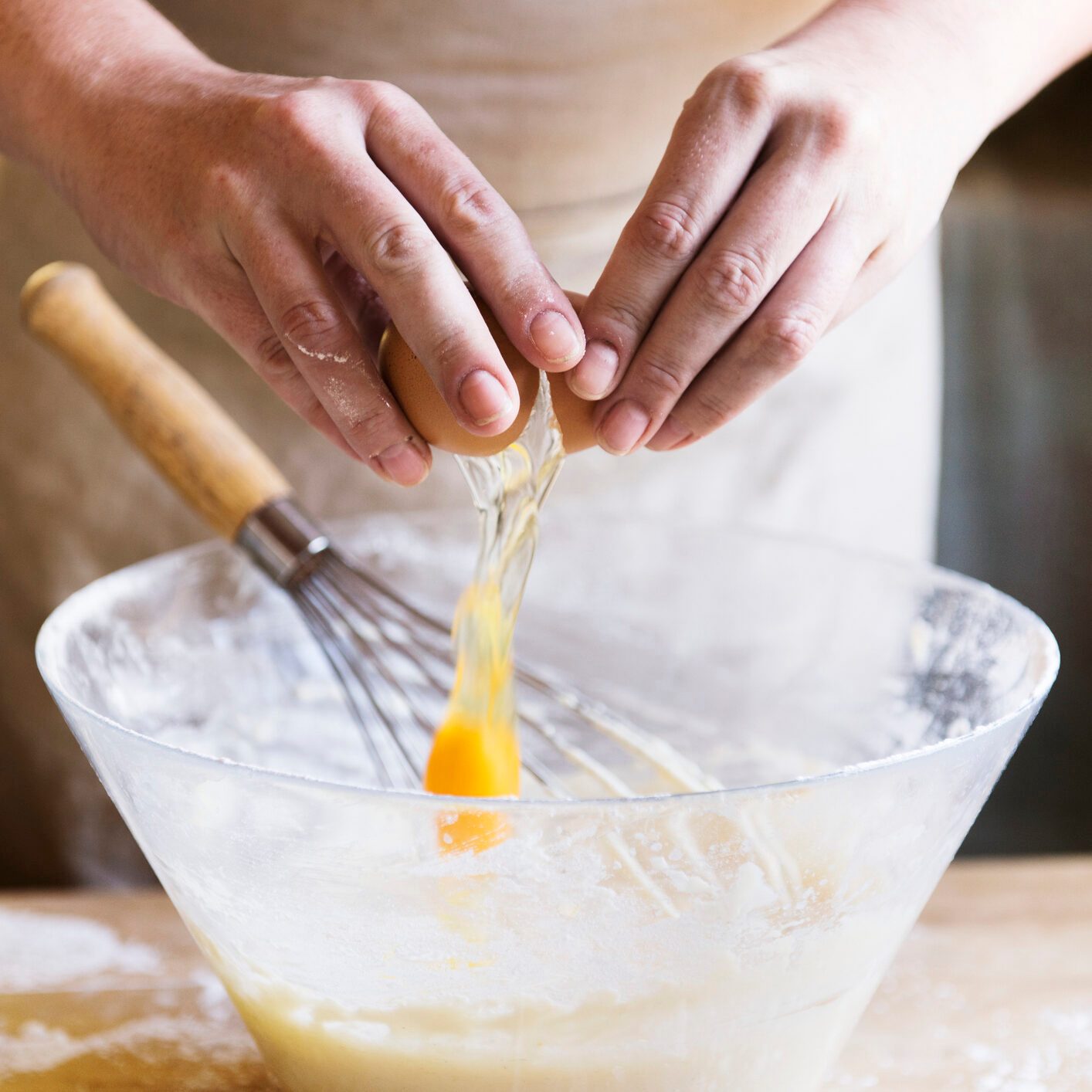 Baker cracking an egg into a bowl of cake batter