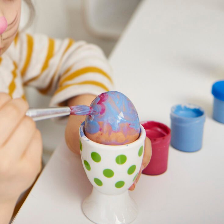 Girl with bunny ears sitting at table painting Easter eggs