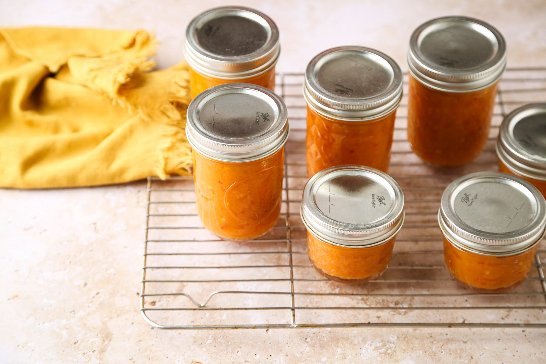 High angle view shot; Place jars into canner with simmering water; ensuring that they are completely covered with water; Bring to a boil; process for 10 minutes; Remove jars and cool on wire rack; yellow napkin; marble surface;