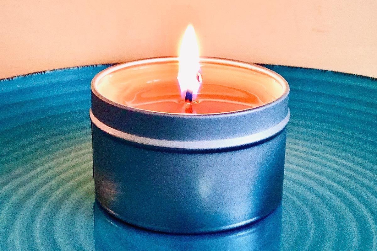 An orange candle in a tin can on a turquoise plate illuminates a peach wall