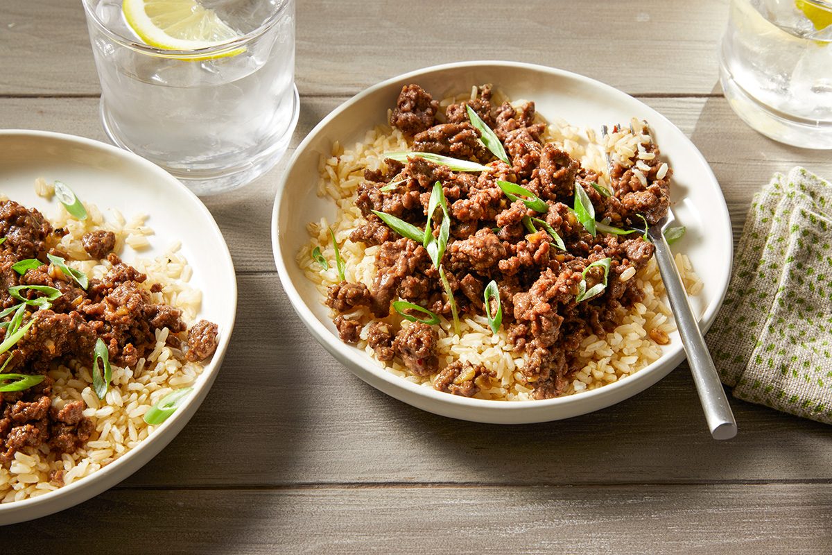 Two bowls of rice topped with cooked minced meat and sliced green onions. 