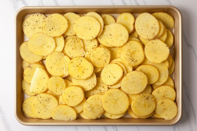 Sliced potatoes seasoned with black pepper and salt are arranged in a single layer on a baking sheet, ready for cooking.