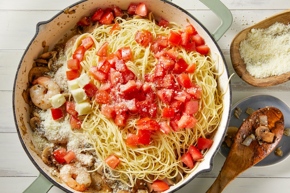 Overhead shot of stir in the tomatoes; 1/4 cup cheese and butter; Drain pasta; toss with shrimp mixture; Sprinkle with remaining cheese; wooden spoon; white wooden surface