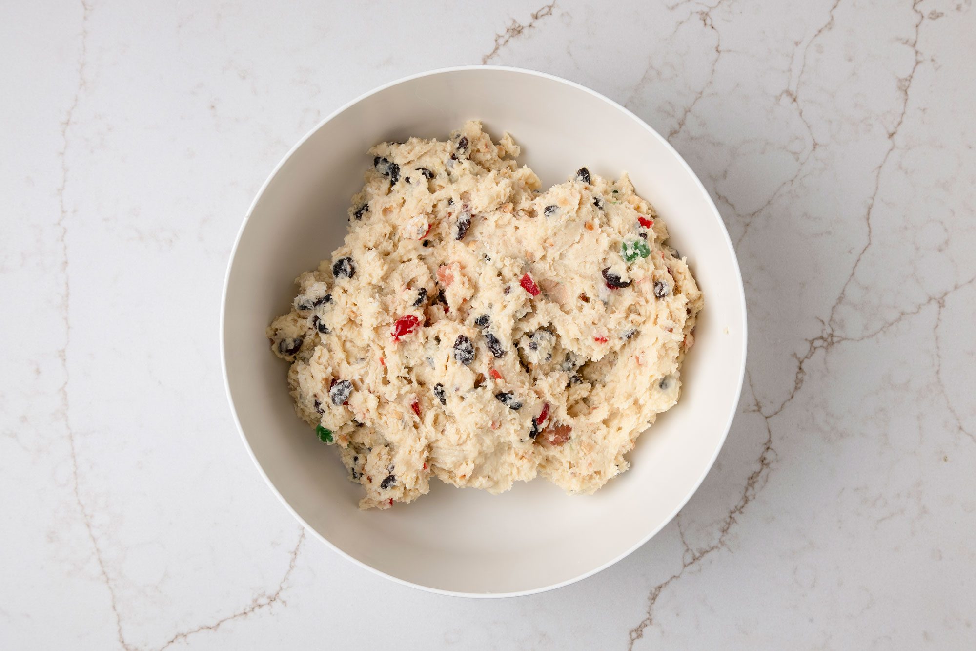 overhead shot of a bowl filled with a thick mixture that appears to be a type of dough or batter; resting on a marble surface