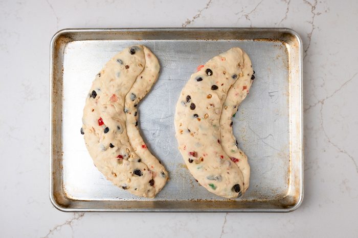 overhead shot of two elongated shapes of dough placed on a baking tray; and the surface below the dough appears to be a light colored marble or stone