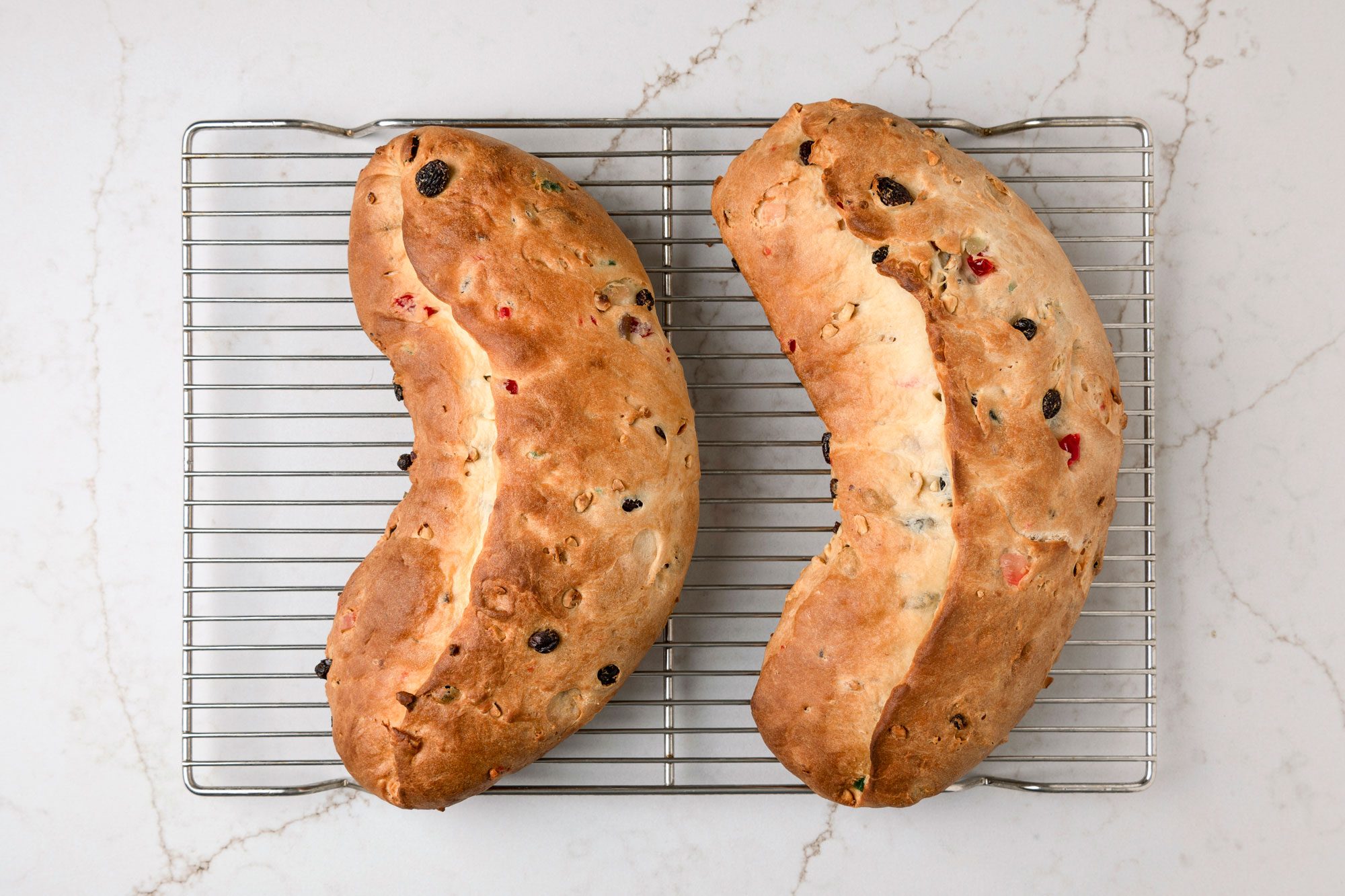 overhead shot of Two loafs of bread resembling a crescent or half moon, The loafs are resting on a wire cooling rack, A light colored countertop
