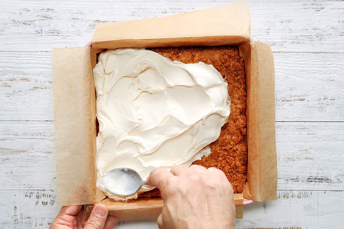 Overhead shot of spread vanilla ice cream onto crust; freeze; covered until firm; white wooden surface;