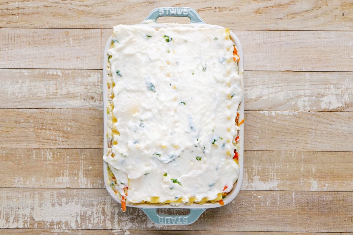 assembled lasagna in baking dish with noodles and white sauce on top