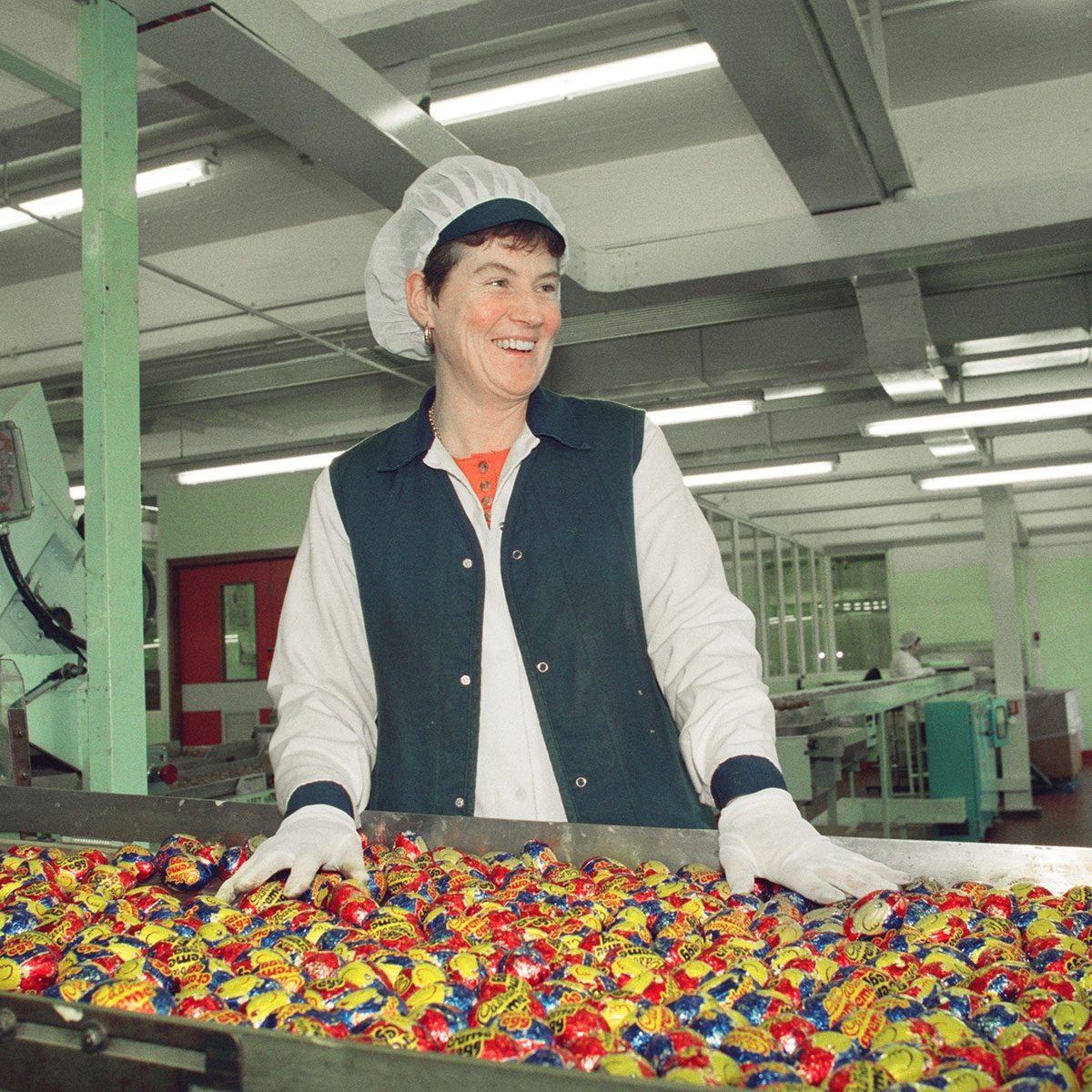 Worker stands behind a conveyor belt of cadbury creme eggs in a factory