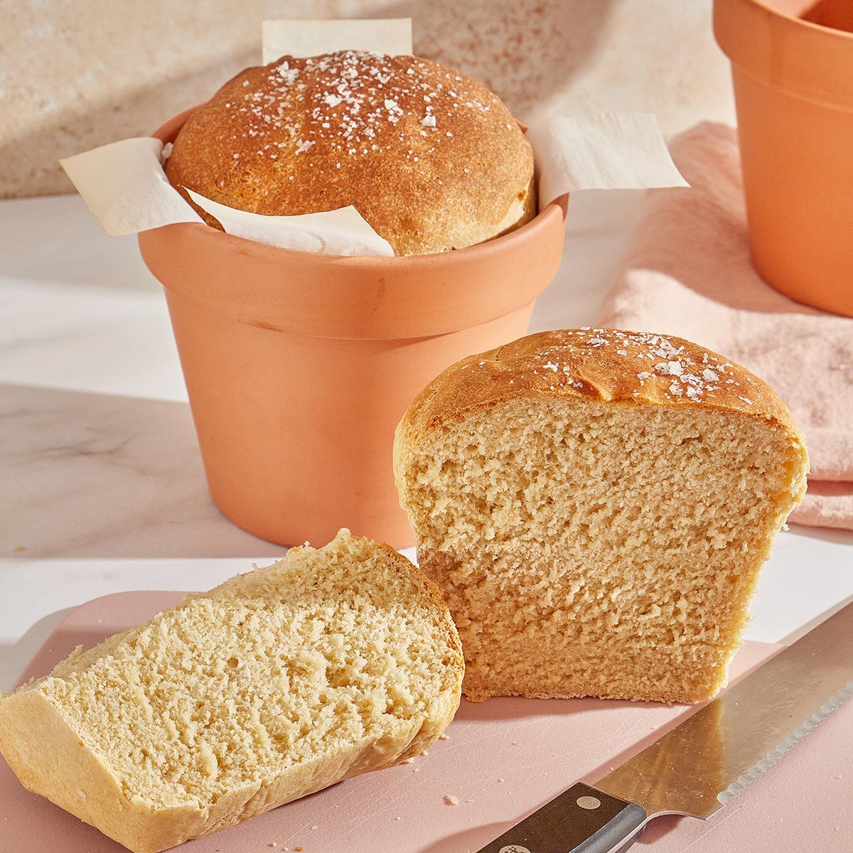 Bread loaf baked in a terra cotta flowerpot with another loaf in front of it sliced in half