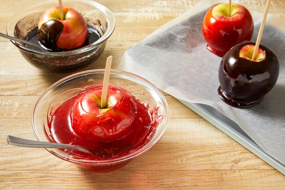 Table view shot of working quickly; dip 2 apples into red sugar mixture; and 2 apples into black sugar mixture to completely coat; Place on prepared baking sheet; let stand until set; light brown surface;