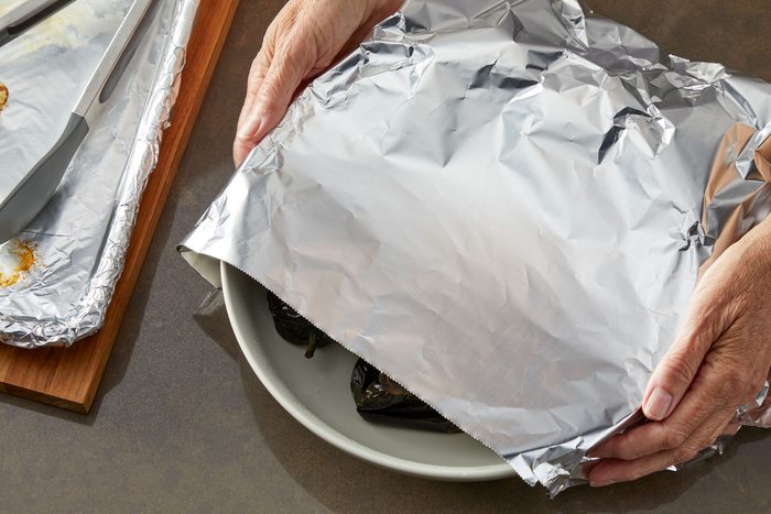 High angle shot; Immediately place peppers in a large bowl; cover and let stand 10 minutes; baking sheet and tongs are placed over wooden board nearby; all set on a light brown surface
