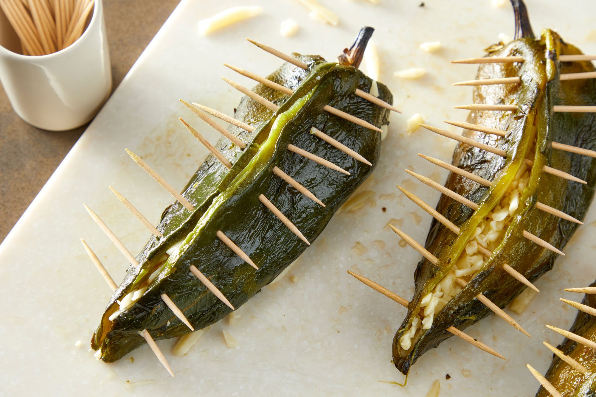 Close shot of stuff peppers with cheese; secure shut with toothpicks; Pour oil into a cast iron skillet 2-inch deep; heat to medium-high; all arranged on a light brown surface