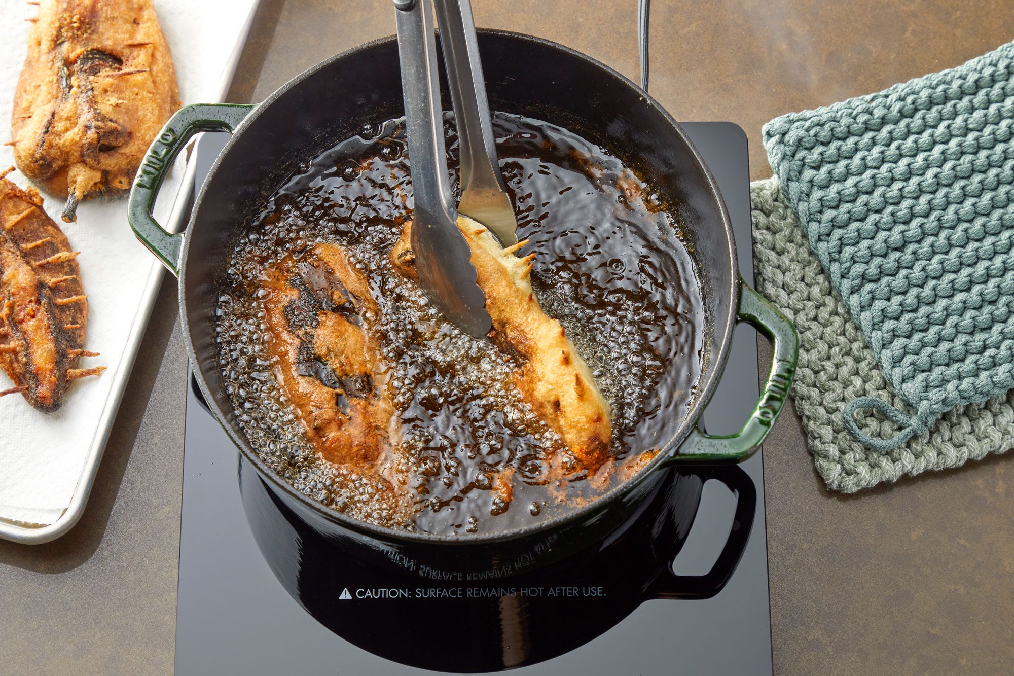 Overhead shot; fry peppers until batter is golden brown and crispy 4-5 minutes per side; Transfer to a paper towel-lined plate or baking sheet to drain; Repeat with remaining peppers; Remove toothpicks from fried peppers; induction; all arranged on a light brown surface