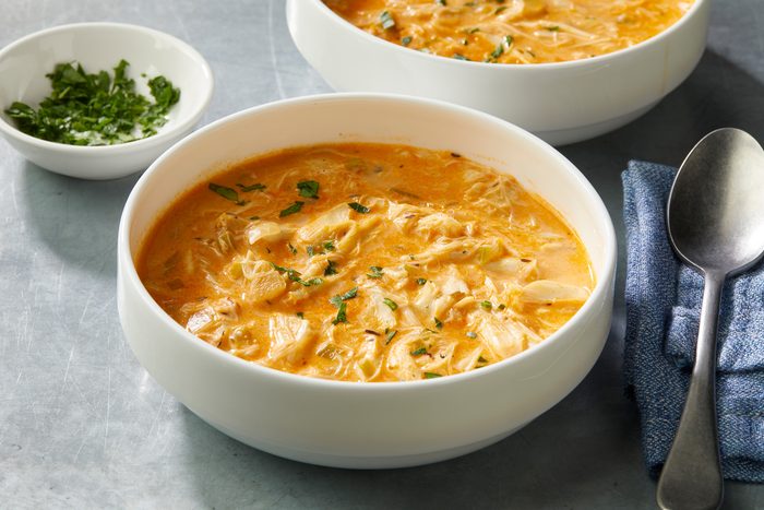 3/4 angle view shot of Homemade Crab Bisque; Served in two large bowls; Garnish with parsley; a spoon rests on a blue napkin; all set on a grey surface;