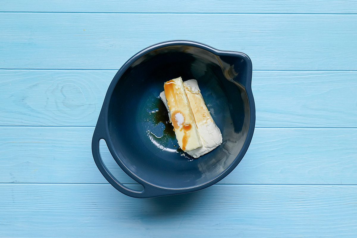 Overhead shot of a large bowl beat cream cheese; butter; vanilla and salt until fluffy; blue wooden surface