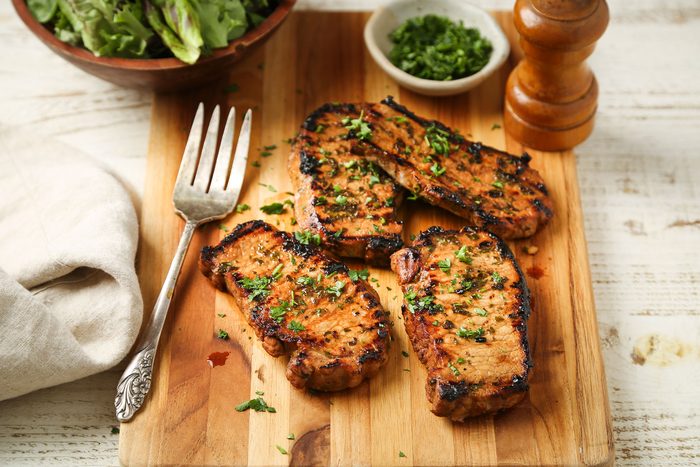 Grilled Boneless Pork Chops on a wooden board with a fork and some greens on side.
