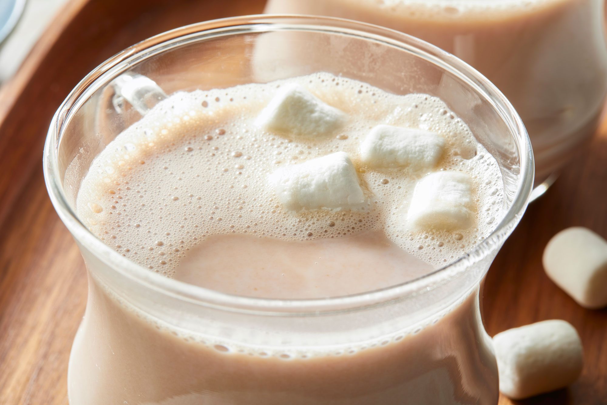 Close-up shot of Fluffy Hot Chocolate; served in glass mugs on a wooden tray; accompanied by a bowl of marshmallows; set on a marble surface