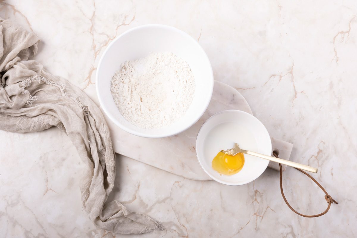 flour in a bowl next to a smaller bowl with beaten egg and milk next to it