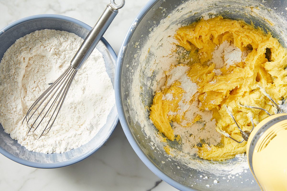 A bowl of flour with a whisk resting beside it, set against a rustic kitchen background.