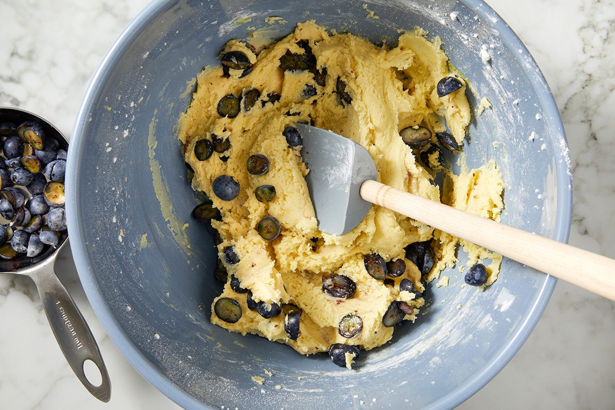 A bowl filled with fresh blueberries next to a metal spatula on a wooden surface.