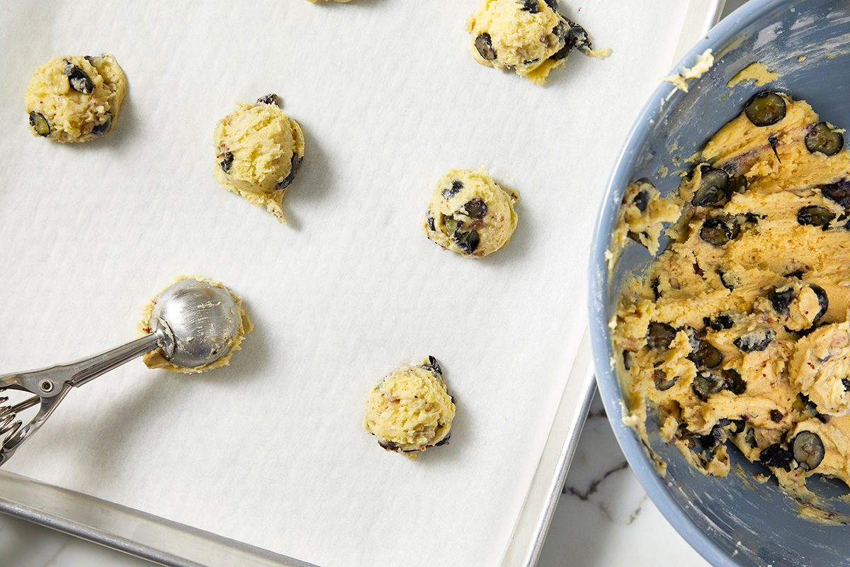 A baking sheet with warm cookies and a spoon, ready for scooping more cookie batter onto the tray.